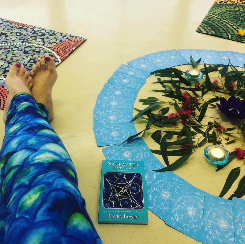 Liz's legs in mermaid tights next to an altar set up for a Qoya class for adults. The altar has eucalyptus leaves and flowers as well as candles and blue oracle cards.  