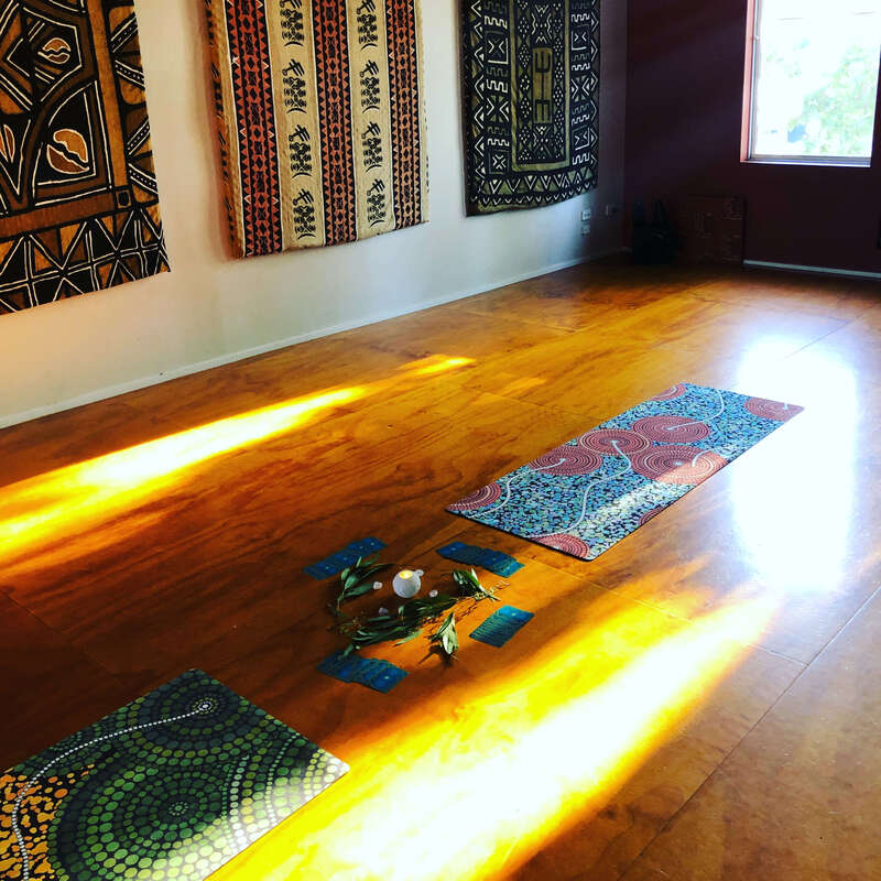 A Qoya class for adults set up at Jibasso studio, above African Drumming in St Kilda, Victoria. There are two yoga mats and an altar  in the centre on a wooden floor. Sun is streaming in from the window. 